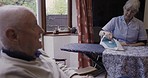 Ironing, laundry and senior couple in conversation during housework, chores and cleaning. Communication, speaking and elderly woman with company from a man during housewife work in the living room