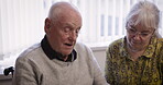 Talking, disability and retirement with a senior couple sitting together in the kitchen of their home. Chatting, wheelchair or love with a disabled man and mature woman bonding in their house