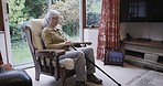Retirement, depression and senior woman in living room by window with memories, nostalgia and thought. Mental health, thinking and sad, lonely and elderly lady in chair in nursing home for Alzheimer