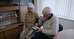Blood pressure, senior care and couple in their home with health measurement machine in living room. Hypertension, reading and elderly man and woman monitoring results for wife with disability