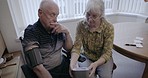 Old couple, blood pressure and medical test in house for cholesterol, hypertension and homecare. Senior people, machine and monitor heart pulse, diabetes risk and cardiovascular wellness in apartment