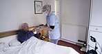 Nurse giving a senior man coffee in bed while healing from covid, flu or a cold in the retirement home. Homecare, medical and mature caregiver with face mask serving warm drink to elderly patient.