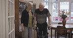 Caregiver, physiotherapy and elderly man with walker in a retirement home disabled in a nursing house. Senior, pensioner and nurse help mature male walk with care, support and healthcare in a lounge