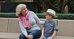 Senior woman and grandson bonding together in a garden with conversation and care. Love, putting on a hat and grandmother relax with family child