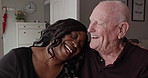 Interracial, senior man and caregiver laugh at home with helping, care and support with retirement and nurse. Smile, living room and hug with happy people in a house with conversation and nursing