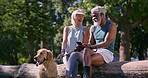 Mature couple, mobile and relax in park with dog, funny message and online shopping on log. Happy man, woman and Golden Retriever with phone for browsing, cute animal blog and care for pet in nature