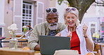 Senior couple, celebration and outdoor with laptop at restaurant for holiday, competition and winning. Happy, man and woman with fist by food at table for achievement email, prize and contest success