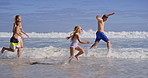 Water splash, parents and kids with running on beach, family vacation and bonding by waves. Playful, mom and dad with children for holiday adventure, connection and happy with holding hands on ocean