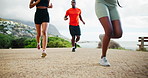 Legs, running and outdoor with group, fitness and low angle on beach promenade by mountain for workout. People, race or marathon training with team, feet and sneakers on ground for exercise in nature