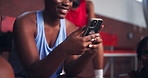 Happy woman, typing and bench with phone for sports app, game or texting on bleachers. Female person, hands and chatting with mobile smartphone for fitness program, news or basketball match on court