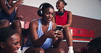 Headphones, sports and woman on bleachers with phone for listening to music, audio and radio. Basketball, team and person on smartphone online to relax after training, exercise and fitness in court