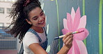 Art, woman and painting on wall in city for creative design, decoration and volunteer with wind. Artist, happy girl and painter outdoor with brush for community mural, floral color or charity project