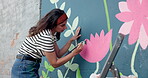 Woman, student and painting mural on wall of creative decoration, community project and artistic freedom. Person, artist and diy with public art, flower design and local culture for therapeutic hobby