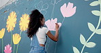 Art, woman and volunteer painting mural on wall for creative design, flower decoration or hobby. Artist, girl and painter outdoor with brush for community project, inspiration and back for charity