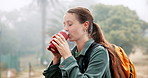 Hiking, woman and drinking coffee in nature on vacation, thinking or relax with fog in winter. Trekking, flask and happy person outdoor with hot beverage, blow tea or travel with reflection in forest