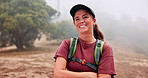 Face, trekking and happy woman in nature with confidence for travel, adventure and holiday with fog. Smile, portrait and female person hiking outdoor for trip, vacation and arms crossed with cap