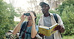 People, friends and book with binoculars in forest for bird watching, adventure or sightseeing in nature. Man, woman or explorers with textbook for journey, information or outdoor expedition in woods