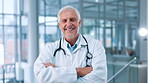 Face, happy man and mature doctor with confidence in hospital for healthcare or cardiology. Smile, physician and medical professional with arms crossed, surgeon and medicine expert with experience