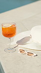 Orange, cocktail and sunglasses with hat by pool for hospitality at summer getaway or resort. Empty, drink or cool mocktail with lemon or shades for weekend vacation, party or vitamin C by poolside
