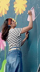 City, woman and artist painting mural for flower decoration, diy and student with creative design outdoor. Art, color and painter with brush on wall for community project, floral hobby and culture