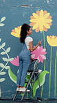 Girl, painting and flowers on wall with smile, mural and art with design for community in urban town. Woman, painter and happy with social responsibility, creative or volunteer for building in Brazil