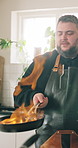 Home, flame and man in kitchen, cooking and enhance flavor with culinary skills. Person, apartment and chef with food, taste and technique with pan on fire, professional and meal prep with cuisine