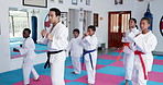 Teaching karate, children and group exercise in dojo for sport, fitness lesson or self defense class. Students, instructor and practice martial arts with man for workout, learning and kids training