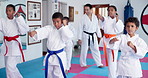 Kids, learning karate and training in class with instructor for fight, fitness or self defense. Students, children and people practice martial arts, kick and exercise for lesson with teacher in dojo