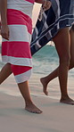 Legs, group and vacation at beach, summer and friends with towel, sunglasses and outdoor by shoreline. People, feet and walking together on holiday, ground and waves on tropical getaway by ocean