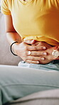 Cramp, hands and stomach pain with person on sofa in living room of home for ibs or indigestion. Condition, discomfort and tender tummy with woman closeup in apartment for abdominal inflammation