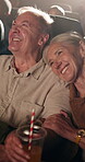 Happy, drink and senior couple in cinema for movie on date together for anniversary celebration. Love, laughing and elderly woman with man cuddle for watching comedy film at theater with beverage.