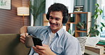 Headphones, cellphone and man with coffee on sofa in home for chatting, relaxing and listening to music. Audio tech, phone and male person with networking and streaming album with tea in living room.