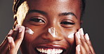 Black woman, face and hands with cream in studio for skincare or beauty on a gray background. Portrait, female person or model with smile, lotion or moisturizer for skin hydration or facial treatment
