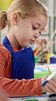 Girl, child and painting on artwork in classroom for creative lesson, art project and motor skills development. Kindergarten, kid student and paintbrush for color activity, education and coordination