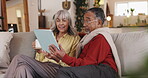 Senior couple, tablet and talking on home sofa with internet connection, browsing and mobile app. Interracial, man and woman with technology for retirement vacation, plan and coffee for conversation