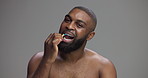 Black man, brushing teeth and face in studio for dental routine, hygiene and wellness by background. Person, model and bamboo toothbrush for sustainability, cleaning mouth and oral care in Nigeria