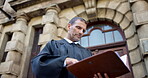 Reading, documents and judge or man in city for trial report, policy legislation and justice guideline. Lawyer review, attorney paperwork and defendant files with mature person at courtroom low angle