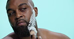 Studio, shaving and man with cream, beard and routine for hygiene in morning and facial treatment. Blue background, grooming and black person with product for hair removal, brush and mockup space