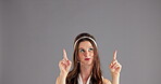 Woman, point up and mockup space for information announcement, feedback for promotion. Person, model and hand gesture in studio on grey background for opinion, deal and excited or good news review