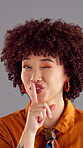 Woman, face and finger to lips for secret, confidential or privacy gesture with wink and afro in studio. African person, quiet or silence signal with mystery news, gossip or rumor on gray background