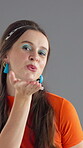 Face, woman and air kiss with fashion, retro makeup and confidence with eyeshadow, flirt and fun on gray background. Smile, portrait and female person with vintage style or blowing gesture in studio