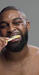 Studio, black man and model with toothbrush for dental, cleaning and oral care with morning routine. Checking, male person and health with teeth whitening for hygiene, wellness and gray background
