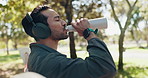 Headphones, fitness and man with water bottle in park for exercise, running and training. Rest, relax and person with liquid for hydration, thirsty and drinking for wellness, health and workout