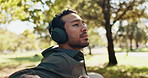 Thinking, relax and man with headphones in park for listening to song, audio and radio outdoor. Resting, calm and person in nature for thoughtful, inspiration and daydreaming with music on bench