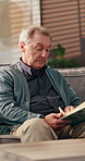 Senior man, reading book and sofa in home, relax and knowledge in retirement with story in living room. Elderly person, novel and literature on couch with poetry, language and lounge at apartment