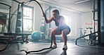 Woman, fitness and gym with battle rope for muscle gain, endurance training or stamina. Active, female person or arm exercise with straps or equipment for workout or physical activity at health club