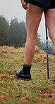 Person, legs and hiking with walking stick on grass field for adventure, journey or outdoor trip. Closeup, hiker or trekking with boots, shoes or aid for physical activity or exercise in forest