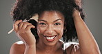 Face, brush and black woman in studio, foundation and confidence on grey background. Portrait, happy person and model with cosmetics tools, aesthetic and skincare with beauty, grooming or dermatology