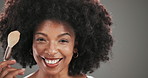 Face, brush and black woman with cosmetics, makeup and foundation on grey studio background. Portrait, happy person and model with beauty tools, aesthetic and skincare with grooming and confidence