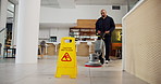 Janitor, man and office with sanitation service, caution sign and wet floor for disinfection. Hygiene, safety and warning for risk, management and cleaner with tile polishing equipment or maintenance